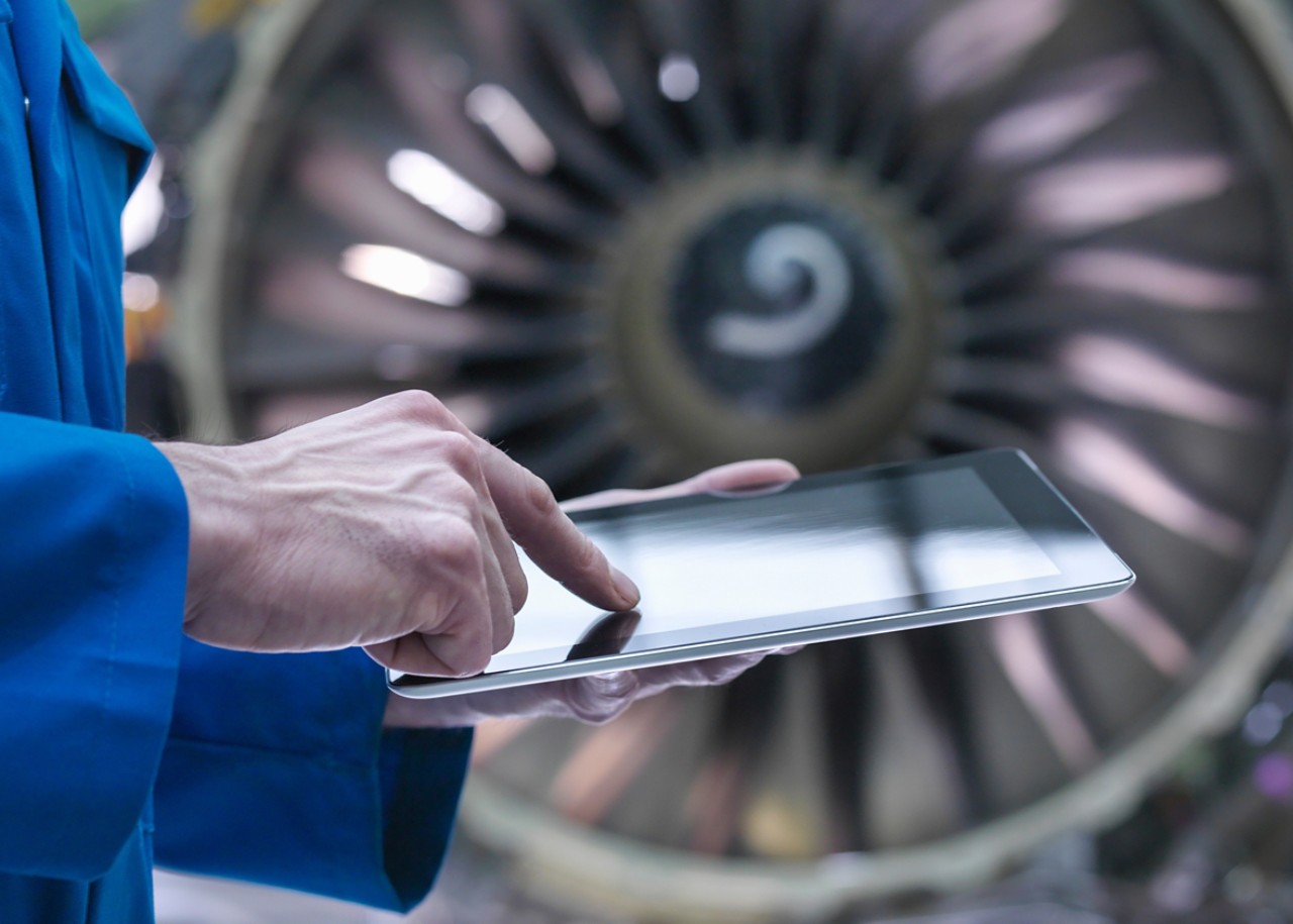 Engineer using digital tablet in front of jet engine in aircraft maintenance factory